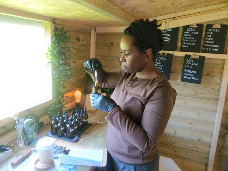 Natalie, a black woman standing inside of wooden room mixing essential oils.
