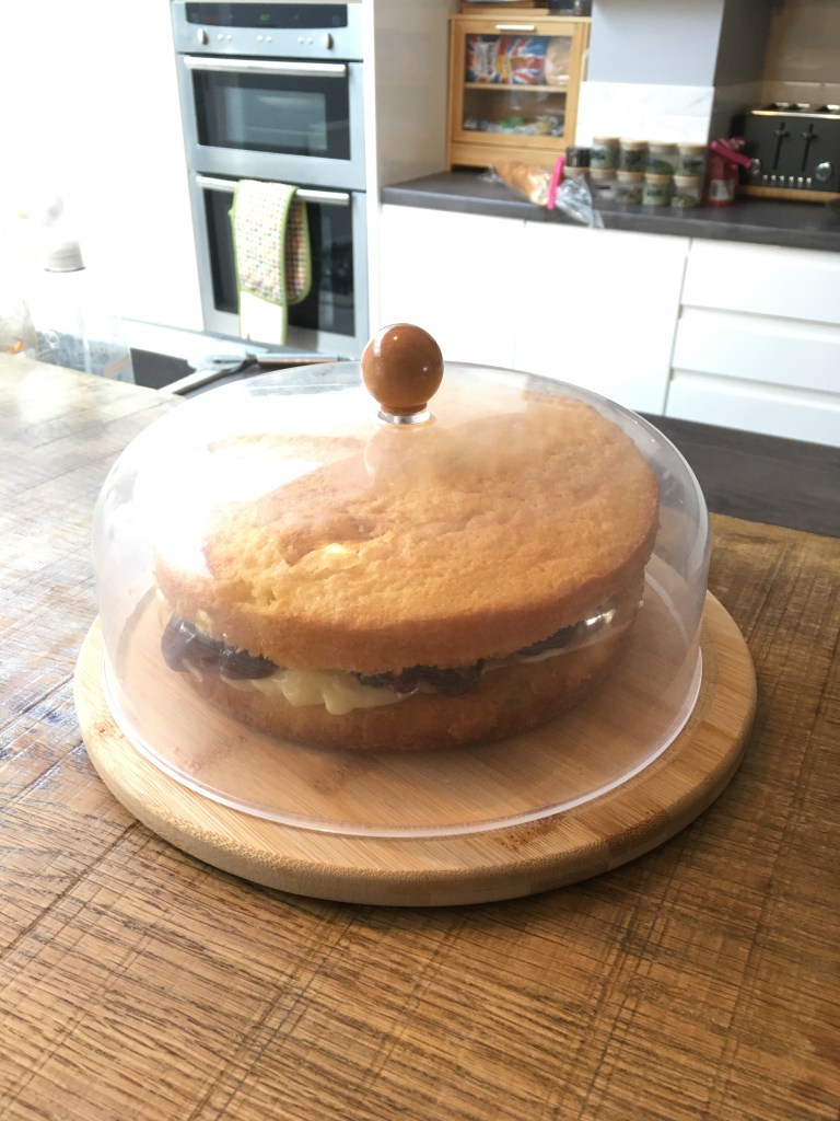 a freshly made victoria sponge under a cake dome in the kitchen