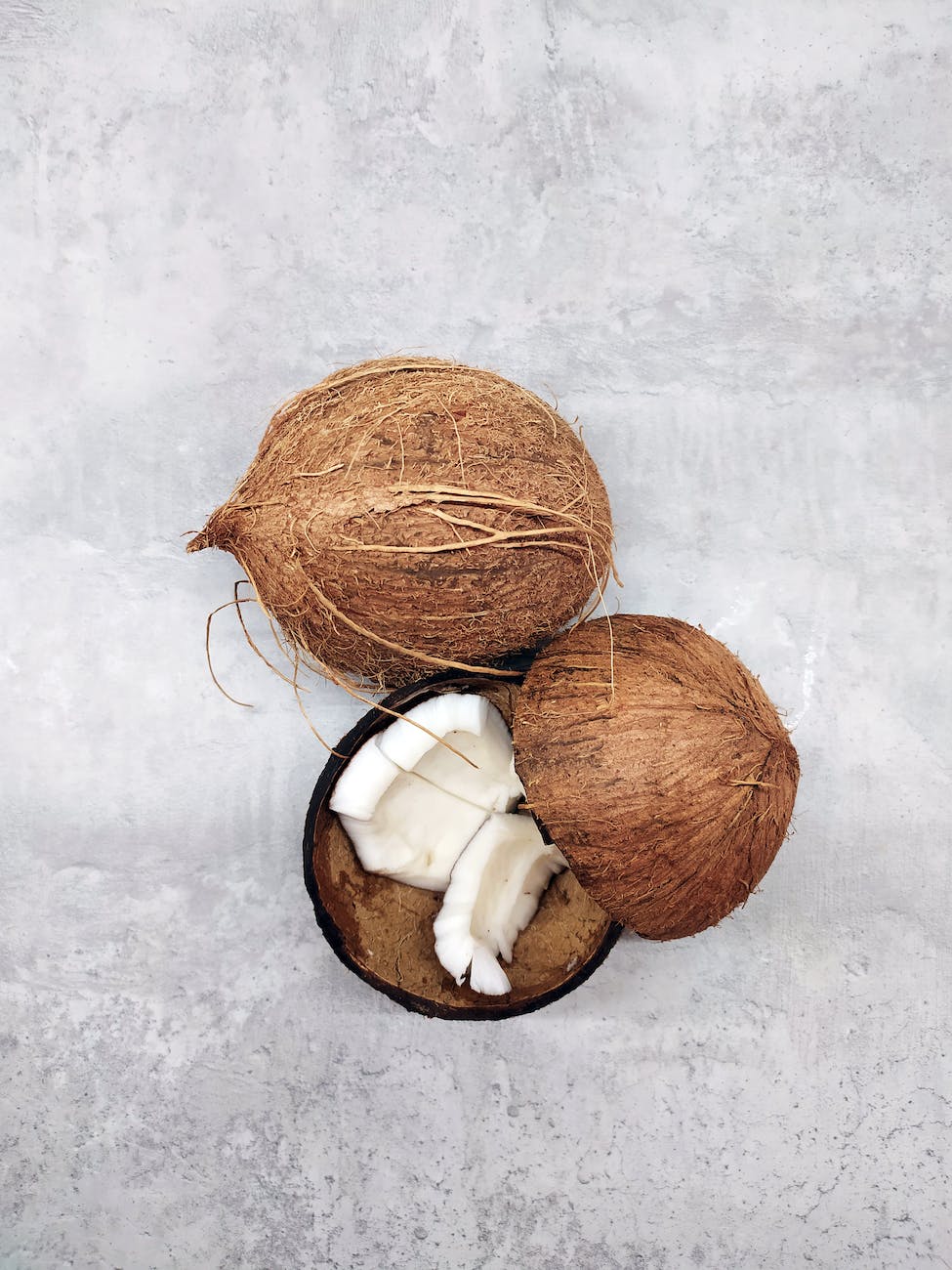 2 coconuts with their husks. 1 coconut is broken in two showing broken white flesh.