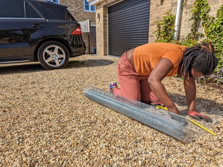 a women on the ground cutting a sheet of wire mesh