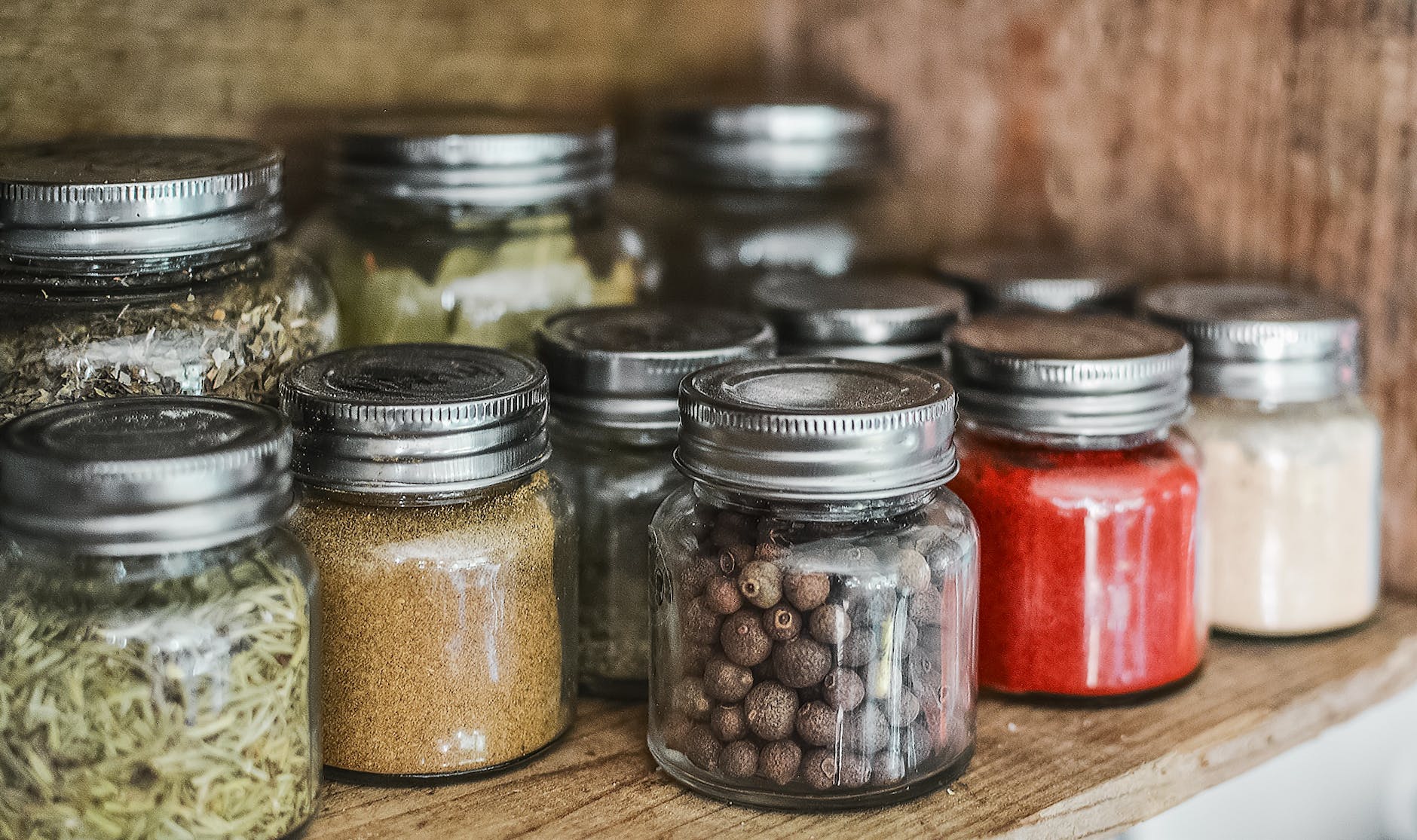 A selection of preserves in clear jars on a shelf in a cupboard.